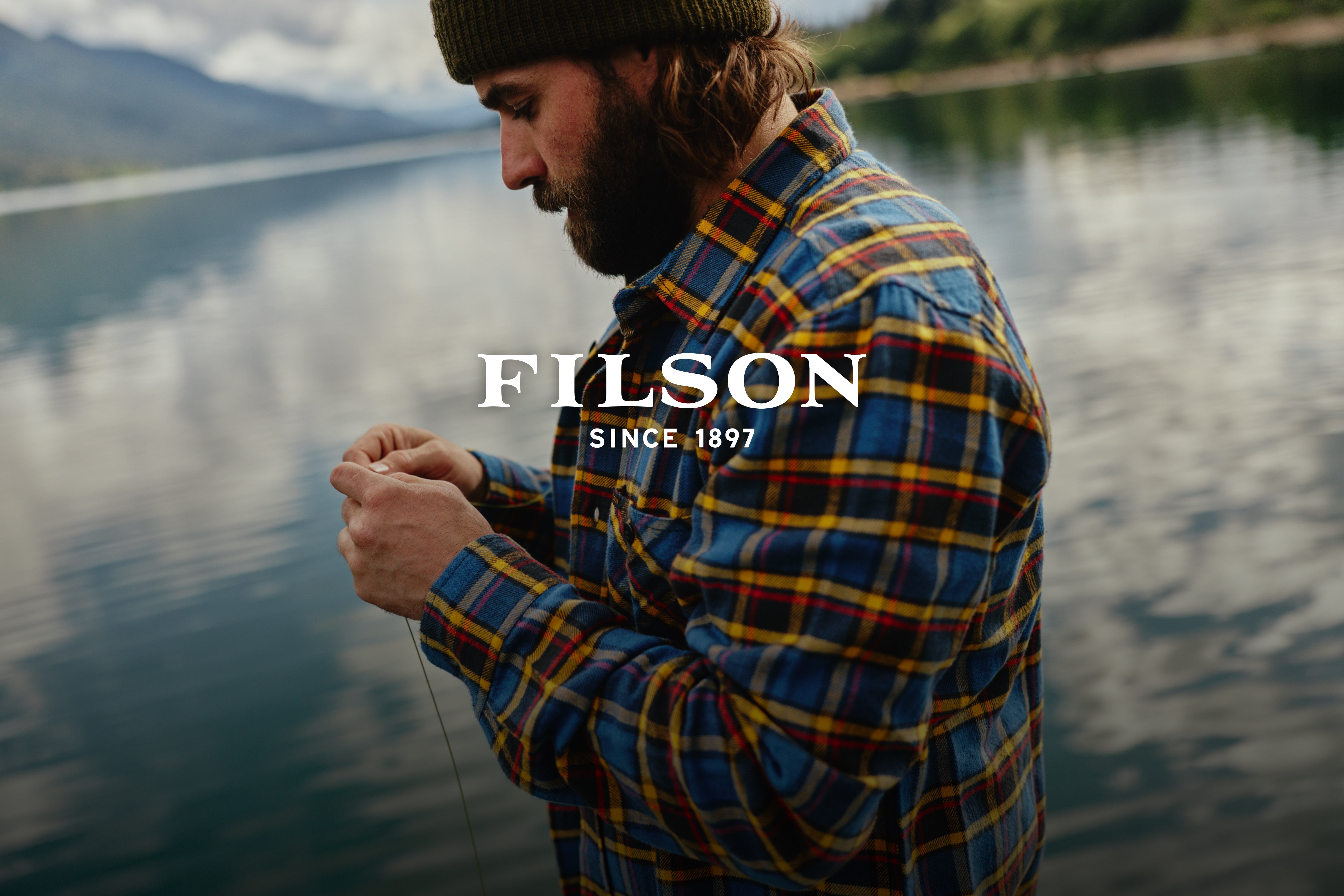 Man wearing a Filson plaid shirt running a fishing line next to a lake